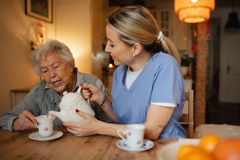 Lovely eldery woman serving tea to friendly caregiver