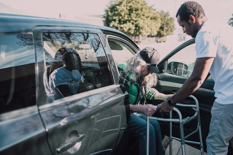 man helping senior out of a car