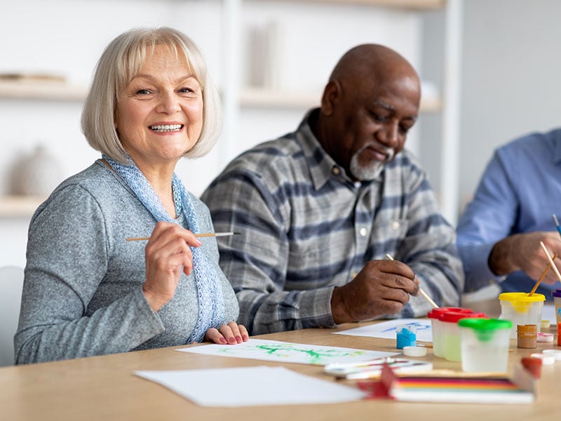 Positive senior woman enjoying painting with brush