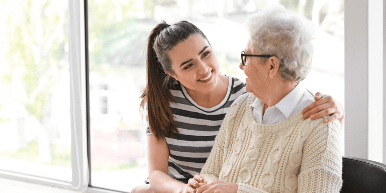 A caregiver sitting with an older woman in a nursing home.