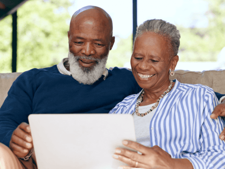 An older couple sitting on a couch looking at a tablet together.